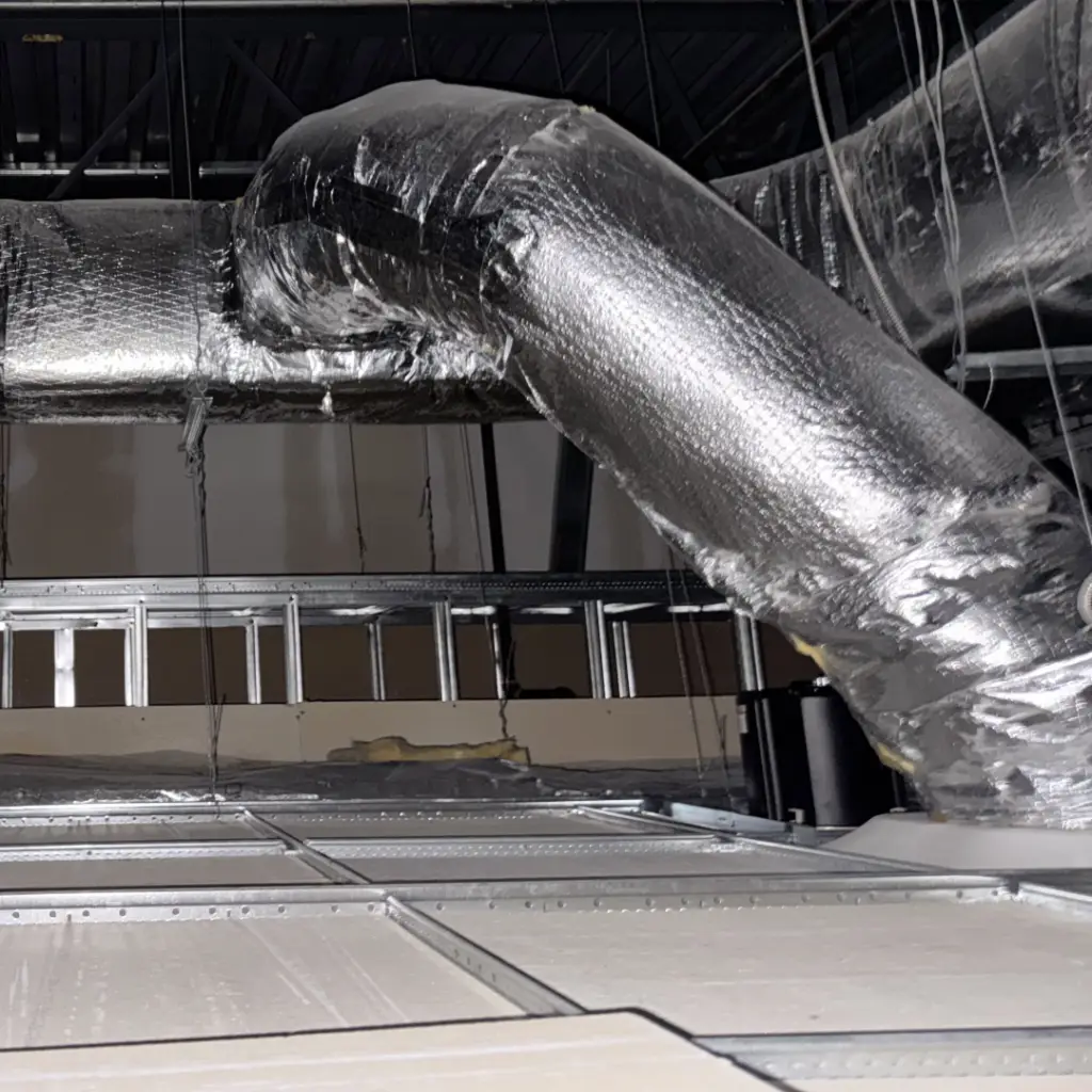 Insulated HVAC supply ductwork installed above a suspended ceiling grid during fit-out