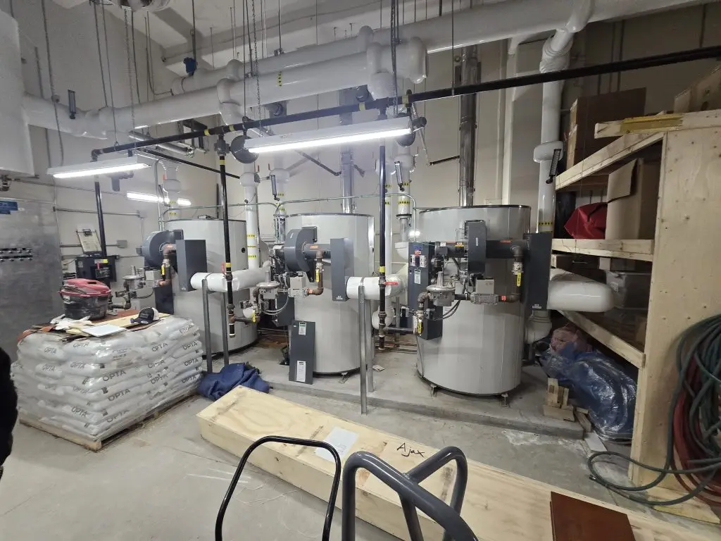 Three replacement commercial water heaters with new gas piping and venting in a mechanical room