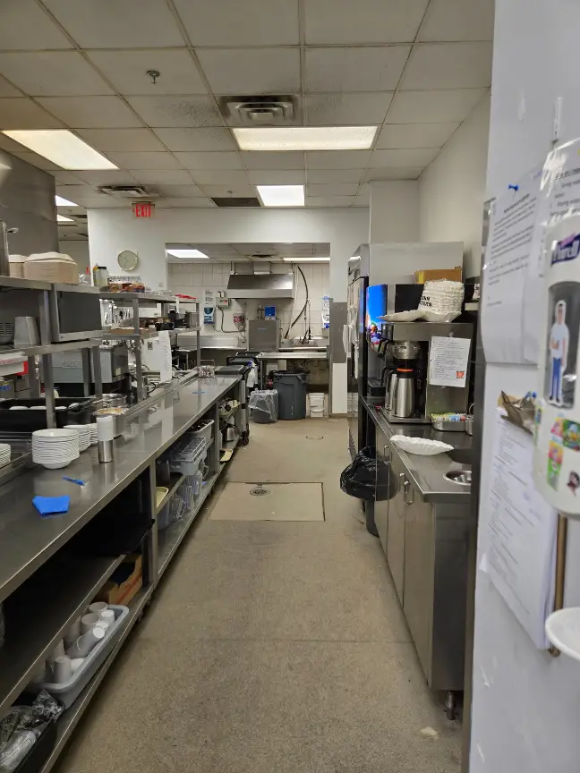 Original commercial kitchen with dated flooring and crowded stainless prep areas before renovation