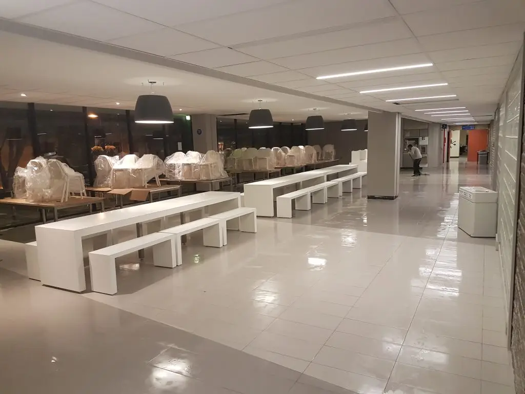 New white benching and tables being installed in a campus common area, furniture still wrapped